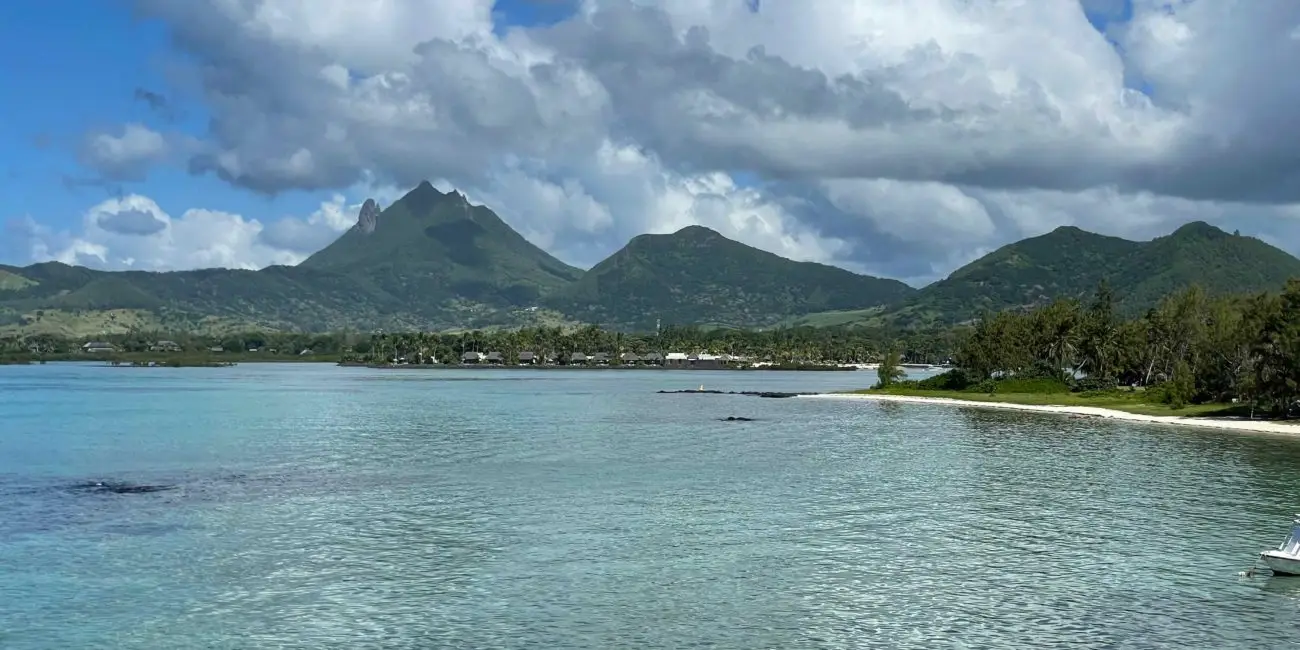 Lagon turquoise de la côte est de l’île Maurice, plage bordée de palmiers et montagnes en arrière-plan